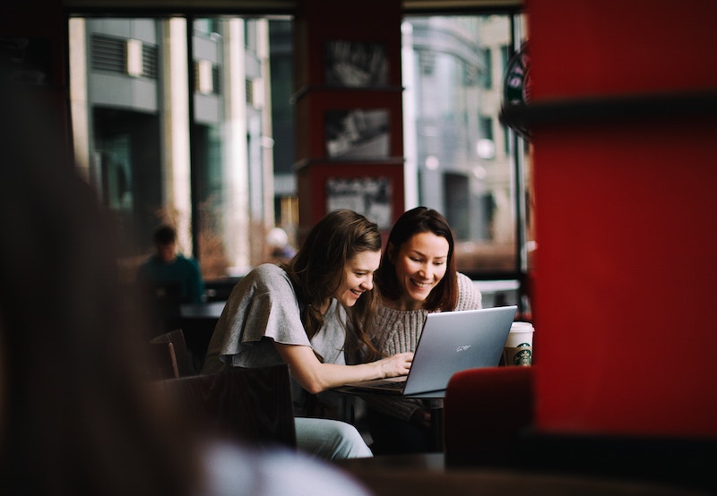 Two women sharing a laptop and laughing.