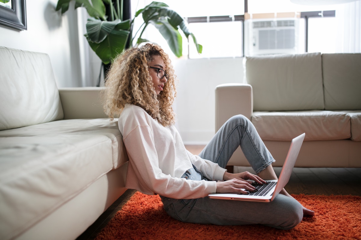 Woman leaning against couch while on laptop.